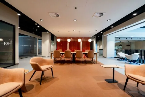 Moderne kantoorruimte aan de Aert van Nesstraat met vergadertafel, sfeervolle verlichting en zithoeken in warme tinten.